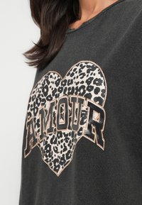 Σκούρο γκρι T-shirt με σχέδιο καρδιάς σε μοτίβο λεοπάρ και τη λέξη «AMOUR» με έντονα μαύρα γράμματα περιγραμματισμένα με χρυσό.