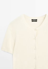 Cardigan court crème à manches courtes en tricot, avec encolure ronde, petits boutons et étiquette Massimo Dutti à l'intérieur du col.