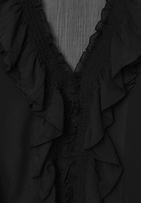 Blusa nera con scollatura a V profonda bordata da volants, dettagli smock lungo la patta e tessuto morbido e testurizzato.