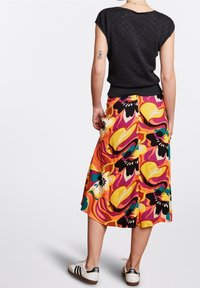 Top negro de manga corta con un patrón texturizado combinado con una falda de longitud media, colorida y con diseños florales en naranja, amarillo y verde.