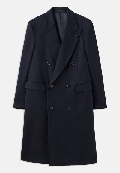 Cappotto doppiopetto navy con revers, realizzato in un materiale simile alla lana. Presenta bottoni neri e tasche frontali. Design minimalista.