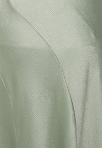 Světle zelená texturovaná látka s jemným leskem, vyznačující se hladkými liniemi a měkkým, jemným spadením. Žádné viditelné vzory ani hardwarové detaily.