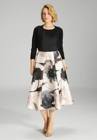 Cardigan negro de manga tres cuartos sobre una blusa negra, combinado con una falda larga y fluida hasta la rodilla que presenta un patrón floral en tonos de rosa y gris.