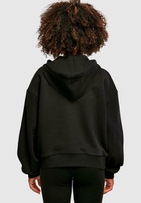 Sudadera negra de gran tamaño con capucha regulable, mangas anchas y dobladillo acanalado. Textura suave, diseño minimalista, adecuada para uso casual.