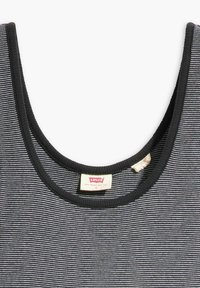 Black and white striped tank top with a rounded neckline and ribbed trim. Features a visible brand label. Soft fabric texture.