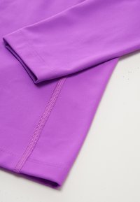 Paarse lange mouw kledingstuk met een gladde, rekbare textuur en platte naden. Bevat een opgevouwen mouw en schone randen. Ideaal voor sportkleding.