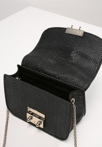 Czarna torebka z fakturą wężowej skóry, srebrnymi okuciami, prostokątną metalową klamrą i długim łańcuszkowym paskiem. Wnętrze widoczne, otwarte.