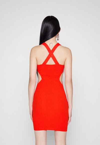 Robe tricotée rouge à côtes avec des bretelles croisées dans le dos et des découpes sur les côtés, présentant une silhouette ajustée qui se termine au milieu de la cuisse. Texture lisse.