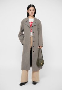 Šedý dlhý kabát s golierom, s prednými gombíkmi, v kombinácii s bielym tričkom a béžovými širokými nohavicami. Súčasťou je zelená taška na crossbody.