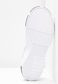 Semelle d'une basket blanche Puma montrant des motifs de bande de roulement texturés et le logo Puma sur un fond blanc immaculé.