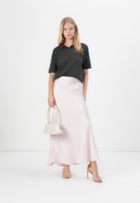 Camisa polo preta de mangas curtas, saia maxi de cetim rosa claro, bolsa bege e sandálias de salto alto com tiras nuas. Texturas suaves e brilho sutil.