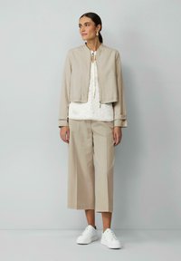 Veste cropped beige sur un blouse blanche à fleurs, associée à un pantalon ample beige clair et des baskets blanches. Tissu lisse, coupe ajustée.