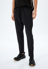 Pantalones deportivos negros con un diseño ajustado, cintura elástica y cordón. Textura suave con bolsillos laterales y un corte moderno.