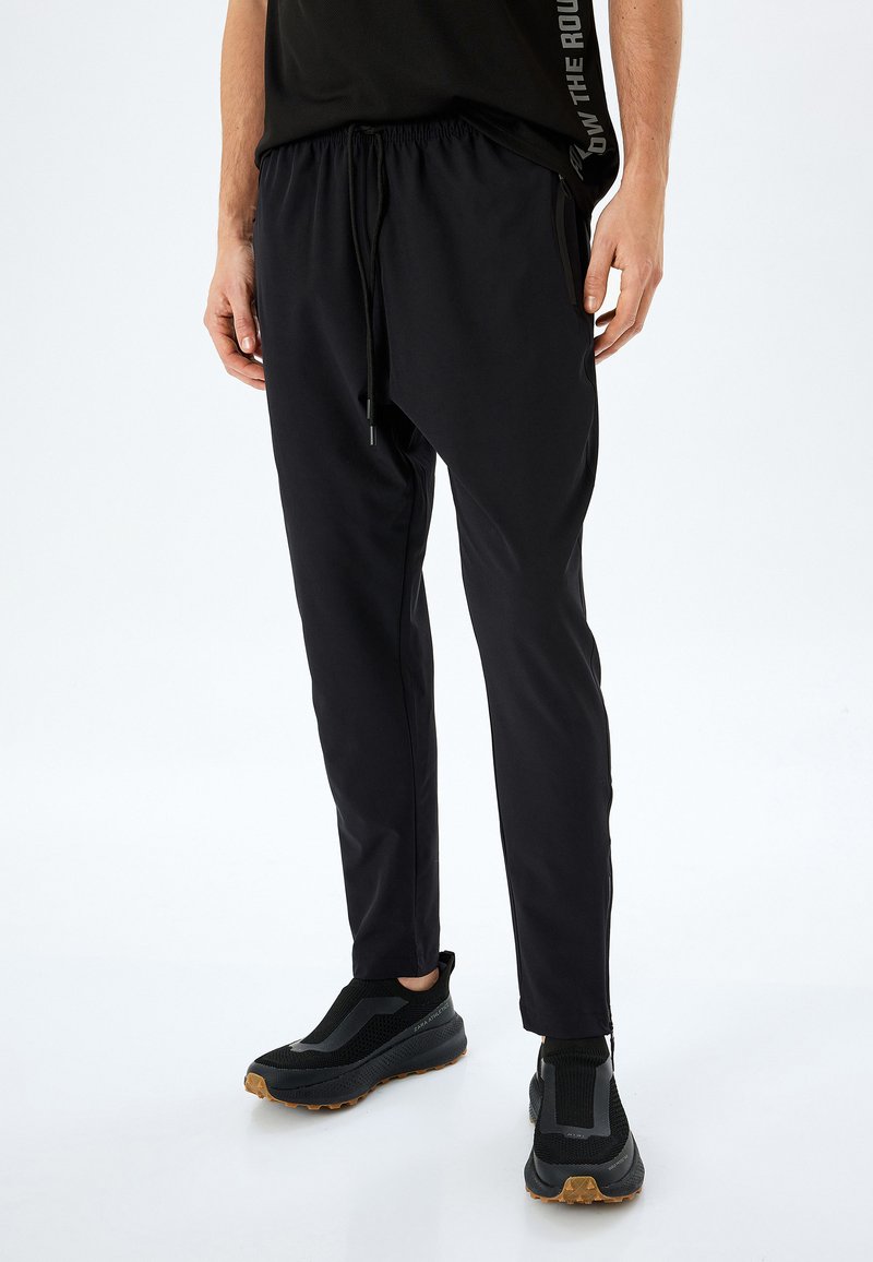 Pantalones deportivos negros con un diseño ajustado, cintura elástica y cordón. Textura suave con bolsillos laterales y un corte moderno.