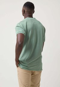 Camisa polo de manga corta en color verde menta, hecha de algodón suave. Presenta un collar clásico y un corte relajado. Se lleva con pantalones beige claros.