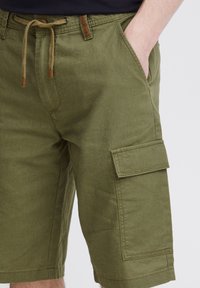 Shorts cargo vert olive en tissu léger ; dotés d'une poche latérale, d'une fermeture à cordon et de détails de couture visibles.