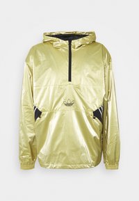 Rompevientos metálico dorado con capucha, media cremallera negra, puños elásticos, bolsillos laterales y logo de Adidas en el centro frontal.