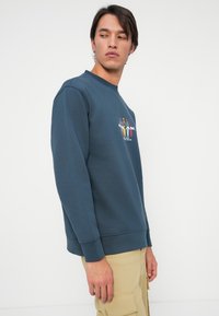 Navyblauwe sweatshirt met een ronde hals, voorzien van een kleurraf grafisch ontwerp van figuren op de borst, gemaakt van zachte fleecestof.