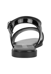 Sandal in pelle verniciata nera con suola piatta, cinturini curvi e chiusura con fibbia laterale. La soletta testurizzata mostra il nome del marchio.