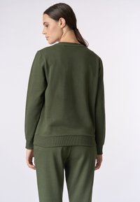 Felpa in cotone verde con collo a giro, polsini e orlo a costine, con una texture liscia. Indossata con pantaloni abbinati, vista da dietro.