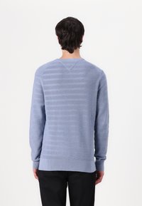 Pulover albastru deschis cu mâneci lungi, dungi texturate orizontale, manșete și tiv cu răsucire, și gât rotund, asortat cu pantaloni negri.