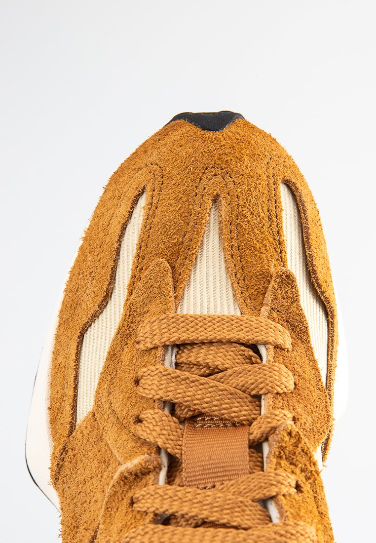 Braune Wildleder-Sneaker mit strukturiertem Obermaterial, cremefarbenen Seitenpaneelen und flachen Schnürsenkeln. Verfügt über auffällige Nähte und eine schwarze Zehenkappe.