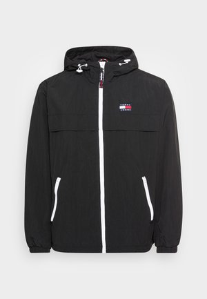Lekka czarna kurtka z kapturem, białym zamkiem błyskawicznym i zameczkami przy kieszeniach, elastycznymi mankietami oraz małym logo Tommy Jeans na piersi.