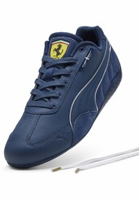 Baskets en cuir bleu marine avec accents en daim, design à lacets, bande argentée, et logo Ferrari jaune sur la languette.
