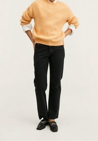 Geel geribbelde gebreide trui, zwarte rechte jeans en zwarte loafers met gouden hardware accenten. De trui heeft opgerolde mouwen en een relaxte pasvorm.