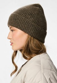 Gorra de punto marrón con canalé y punta encima, exhibida en la cabeza de un modelo de perfil. El material parece suave, con una textura que proporciona calor.