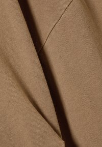 Καφέ υφασμάτινη ύλη με υφή και απαλό, πλεκτό εμφανισιακό χαρακτήρα. Διαθέτει ελαφριά γυαλάδα και ορατές ραφές κατά μήκος των ραφών.