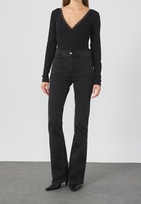 Zwart bodysuit met lange mouwen en kanten rand bij de halslijn, gecombineerd met zwarte, hooggetailleerde jeans met uitlopende pijpen. Beide items hebben een gladde textuur.