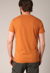 Korte mouwen, ronde hals t-shirt in gebrand oranje katoen, gladde textuur, getailleerde pasvorm, geen patronen of accenten zichtbaar.