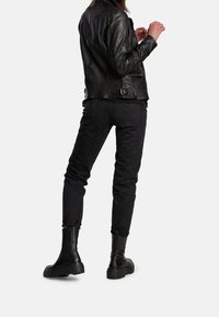 Svart skinnjacka med figurnära passform, kombinerad med svarta jeans och svarta ankle boots. Outfitten har en texturerad yta och minimalistiska metalldetaljer.