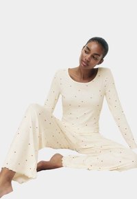 Pyjamasett i krämfärg med långärmad tröja och lösa byxor, med små röda hjärttryck, ribbad struktur och vågiga kanter.