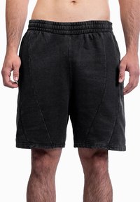 Torso masculino vestindo calções atléticos com cintura elástica preta e bolsos laterais, em pé contra um fundo branco.