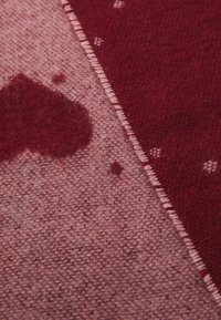 Material tricotat roșu și roz, cu un model de inimioare și puncte mici. Textura este moale, cu un finisaj ușor pufos.