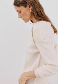 Pull en tricot rose clair avec des détails en côtes sur les épaules et les poignets. Présente des boutons sur les côtés et un tissu doux et texturé.