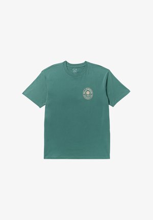 Tavaszi, rövidujjú póló tealevél színű pamutból, bézs színű, kerek logónyomattal a bal mellrészen. Klasszikus crew nyak és laza fazon.