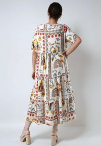 Vloeiende, witte midi-jurk met kleurrijke, retro prints van bloemen, harten en regenbogen; korte mouwen en een gelaagde zoom; gecombineerd met block-heeled sandalen.