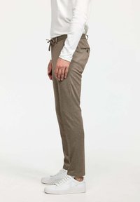 Pantalons marron texturés avec une taille à cordon, des poches latérales et une coupe slim, portés avec des baskets blanches et un haut à manches longues.