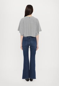 Maglione grigio a maniche corte e taglio corto, abbinato a jeans svasati blu scuro con un sottile dettaglio di cucitura e tasche posteriori.