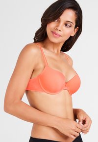 Sostén naranja acolchado con tirantes ajustables, copas sin costuras, un adorno central y una textura suave. Diseñado para comodidad y soporte.