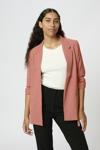 Blazer z jemného růžového materiálu, s upraveným střihem, klopami a dvěma předními kapsami, kombinovaný s bílým žebrovaným topem a černými kalhotami.
