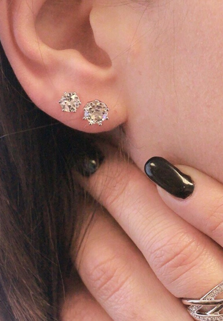 Silberne Steckerohrringe mit zwei klaren, runden Kristallen unterschiedlicher Größe, in Vierverschlusshalterungen gefasst, die an einem Ohr getragen werden.