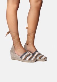 Espadrilles de cu�ña con suela de yute trenzado, que cuentan con un upper de ganchillo en franjas blancas, grises y marrones, y un lazo en el tobillo en forma de cruz.