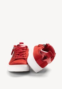 Sneaker di camoscio rosso con suole in gomma bianca, dotate di lacci frontali, cerniere laterali e una linguetta sul tallone. Accentuate da dettagli rossi lucidi.