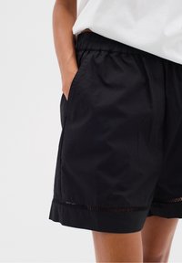 Černé šortky s elastickým pasem, postranními kapsami a lemem s vodorovným vystřižením. Vyrobené z lehkého materiálu.
