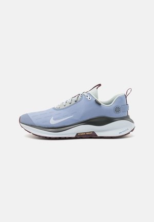 Jasnoniebieski but do biegania Nike z białym znakiem, czarno-białą podeszwą, szarymi sznurowadłami oraz napisem „Storm-Tread” z boku.