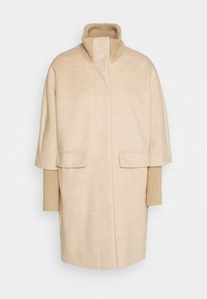 Manteau beige en chevrons avec col roulé en maille côtelée et longs poignets côtelés, poches avant à rabat et fermeture frontale dissimulée.